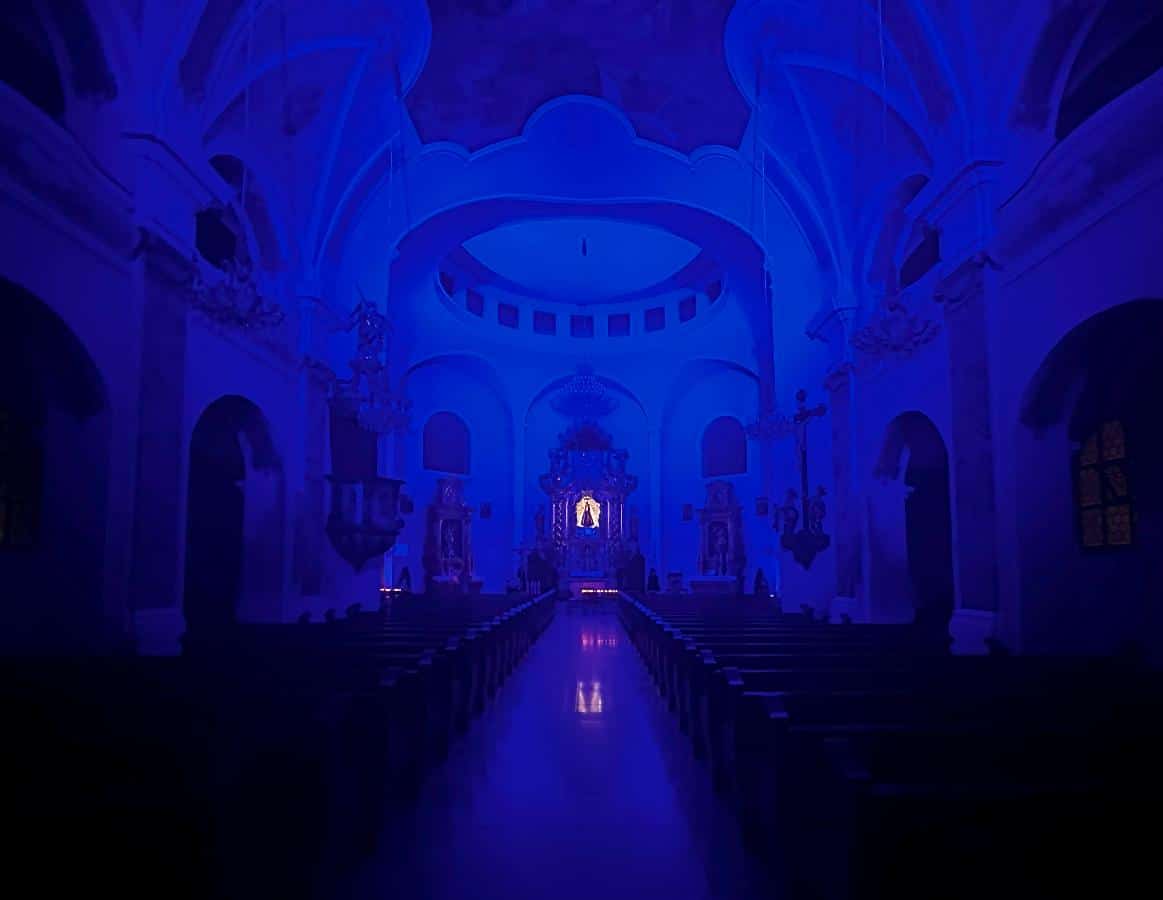 Das schwach beleuchtete Innere der Kirche erstrahlt in blauem Licht, das den Altar im hinteren Bereich hervorhebt.