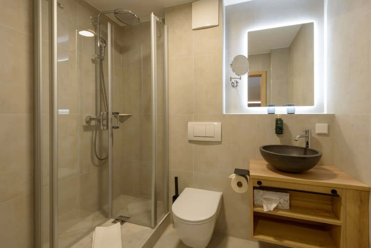 Modernes Badezimmer mit Glasdusche, wandmontierter Toilette, Gefäßwaschbecken und großem beleuchtetem Spiegel.