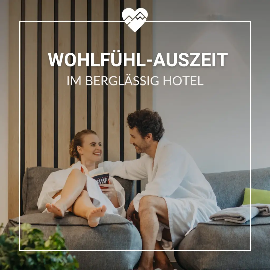 Ein lächelndes Paar in weißen Gewändern entspannt sich auf einem Sofa in einem modernen Hotel, darüber der Text "Wohlfühl-Auszeit".
