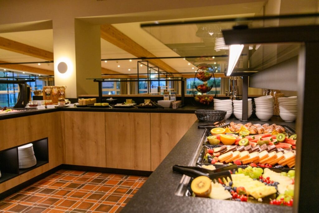 Ein Buffet mit verschiedenen Obstsorten, Gebäck, Aufschnitt und Tellern in einem modernen, hellen Essbereich.