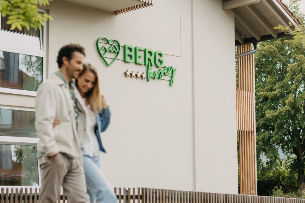 Ein Paar geht an einem Geb&auml;ude mit einem gr&uuml;nen Schild mit der Aufschrift BERG" und einem Herz- und Berglogo vorbei.