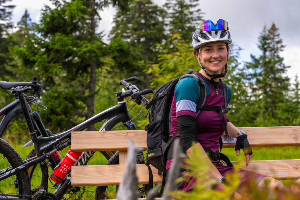 Mountainbikerin macht Pause auf einer Bank im Bayerischen Wald