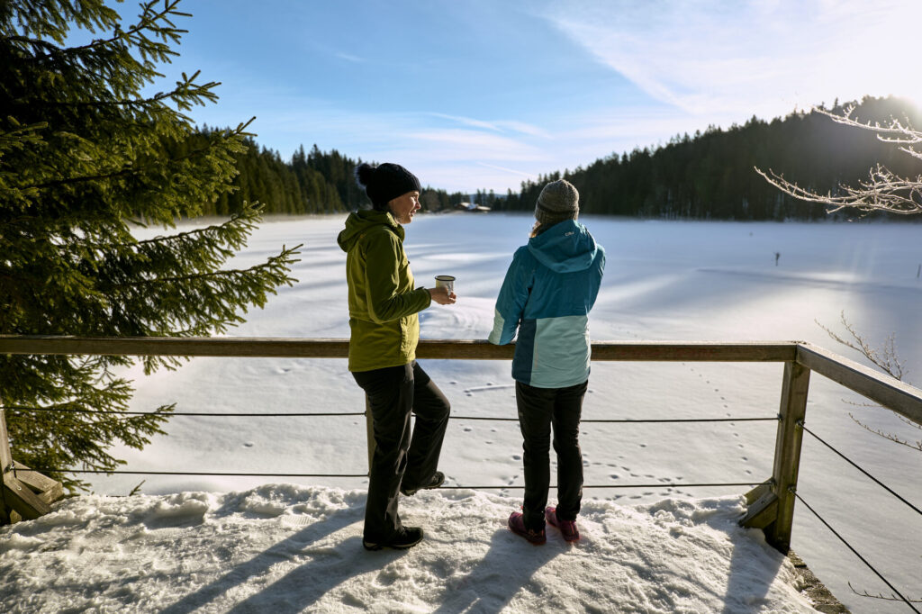 Zwei Winterwanderer mit Blick auf den verschneiten See im Bayerischen Wald